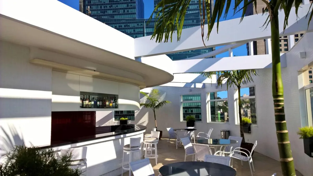 Bar da cobertura do Hotel Atlântico Tower com palmeiras e os prédios do Centro do Rio ao fundo